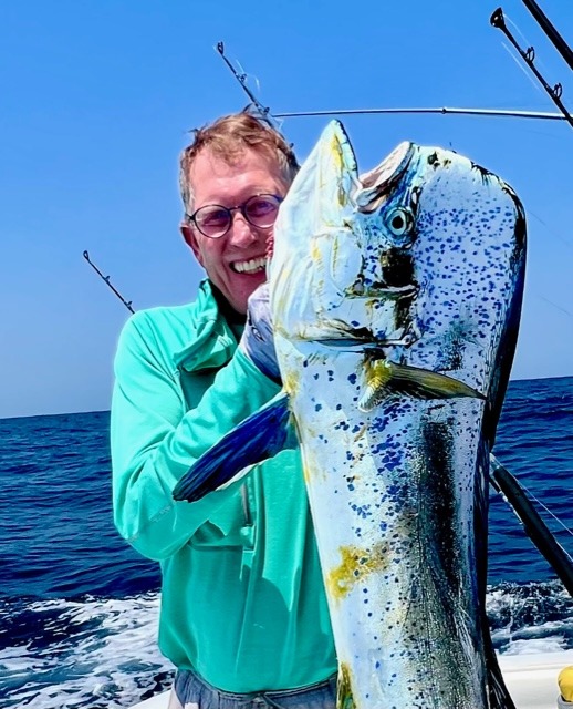 An angler in a green shirt with a colorful catch